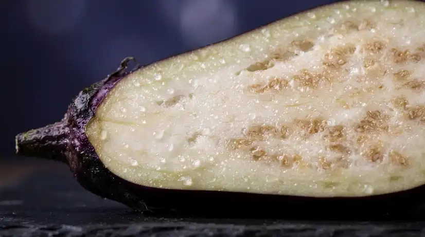 Macro photography of sliced Korean eggplant showing vibrant purple skin, cream flesh, and water droplets reflecting light